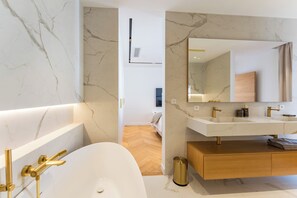 Un bagno moderno con una vasca freestanding, un mobile lavabo con specchio e pareti in marmo.