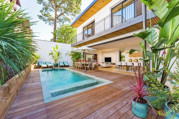 Una casa moderna con un patio in legno, una piscina e mobili da esterno.