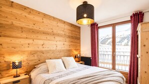 Een slaapkamer met houten lambrisering, een bed, twee bedlampen, een raam met uitzicht op een berg en een hangende lamp.