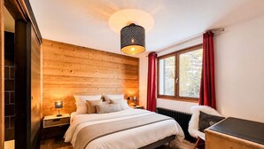Een slaapkamer met een houten wand, een bed met wit beddengoed, een bureau en een raam met rode gordijnen.