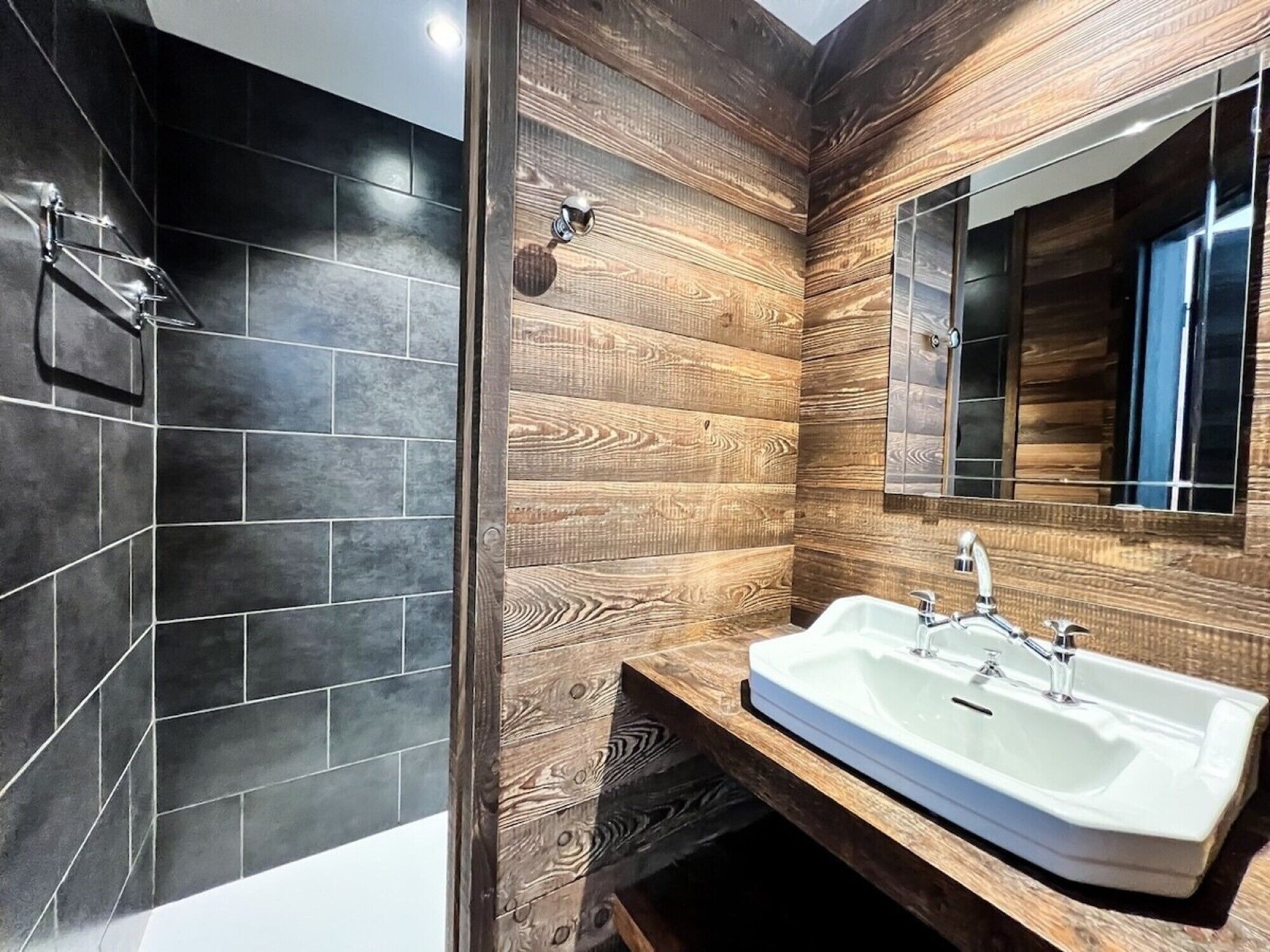 A modern bathroom with a large mirror, a white sink, and a shower area.