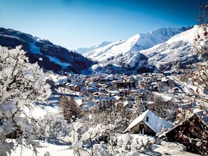 Ein verschneites Dorf mit traditionellen Gebäuden, Bergen im Hintergrund und einem klaren Himmel.