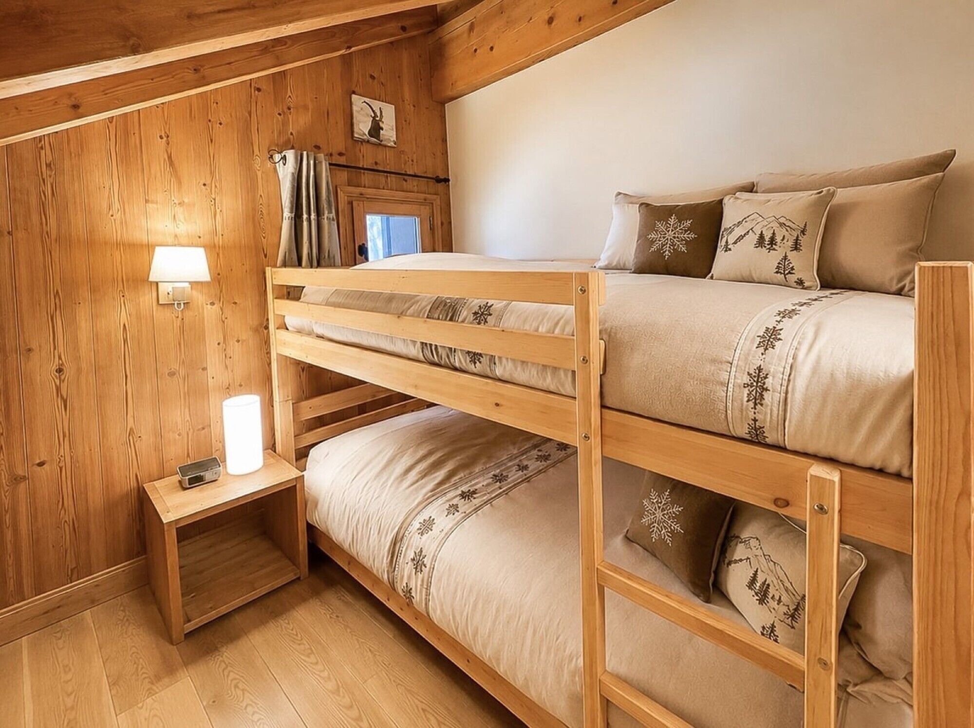 A bunk bed room with wooden walls, a bedside table with a lamp, and a window with curtains.