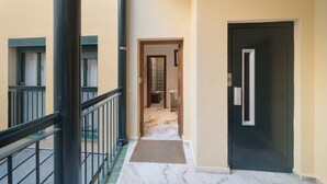 Um corredor com chão de mármore, uma porta preta e uma janela com cortina.