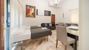Quarto de hotel com duas camas, um sofá, uma mesa de jantar e um candelabro.
