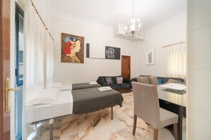 A hotel room with two beds, a sofa, a dining table, and a chandelier. - 'Wellhome Sevilla Centro' Apartment with Wi-Fi, Parking, and Air Conditioning (Seville)