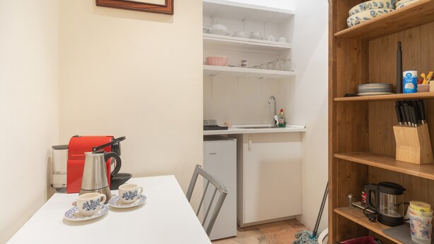 Uma cozinha compacta com uma mesa branca, uma cafeteira vermelha e uma geladeira.