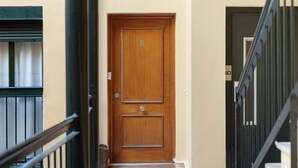 Uma porta de madeira com a letra 'B' em cima, um corrimão de metal e uma janela com cortina.