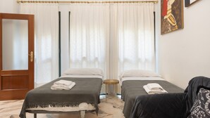 Quarto de hotel com duas camas, porta de madeira, janela com cortinas e um quadro na parede.
