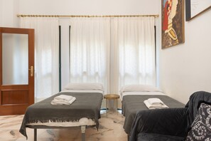 A hotel room with two beds, a wooden door, a window with curtains, and a painting on the wall. - 'Wellhome Sevilla Centro' Apartment with Wi-Fi, Parking, and Air Conditioning (Seville)