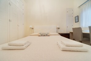 A neatly made bed with two pillows, a bedside table, a chair, and a wardrobe with louvered doors. - Apartment 'Wellhome Sevilla Centro' with Wi-Fi, parking (€20) and air conditioning (Seville)