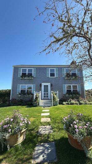A two-story house with a front entrance, a pathway leading to the door, and flower pots on either side.