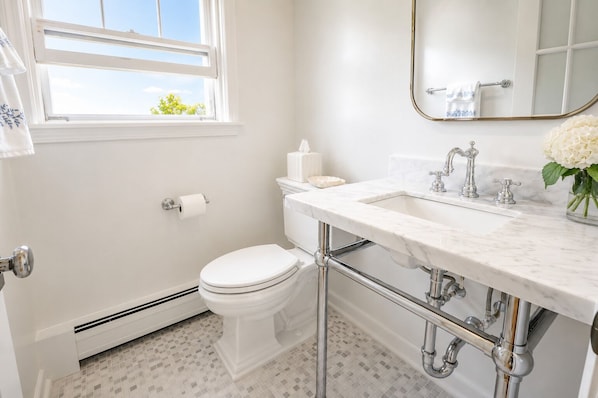 A bathroom with a toilet, sink, mirror, and a window with a view of trees.