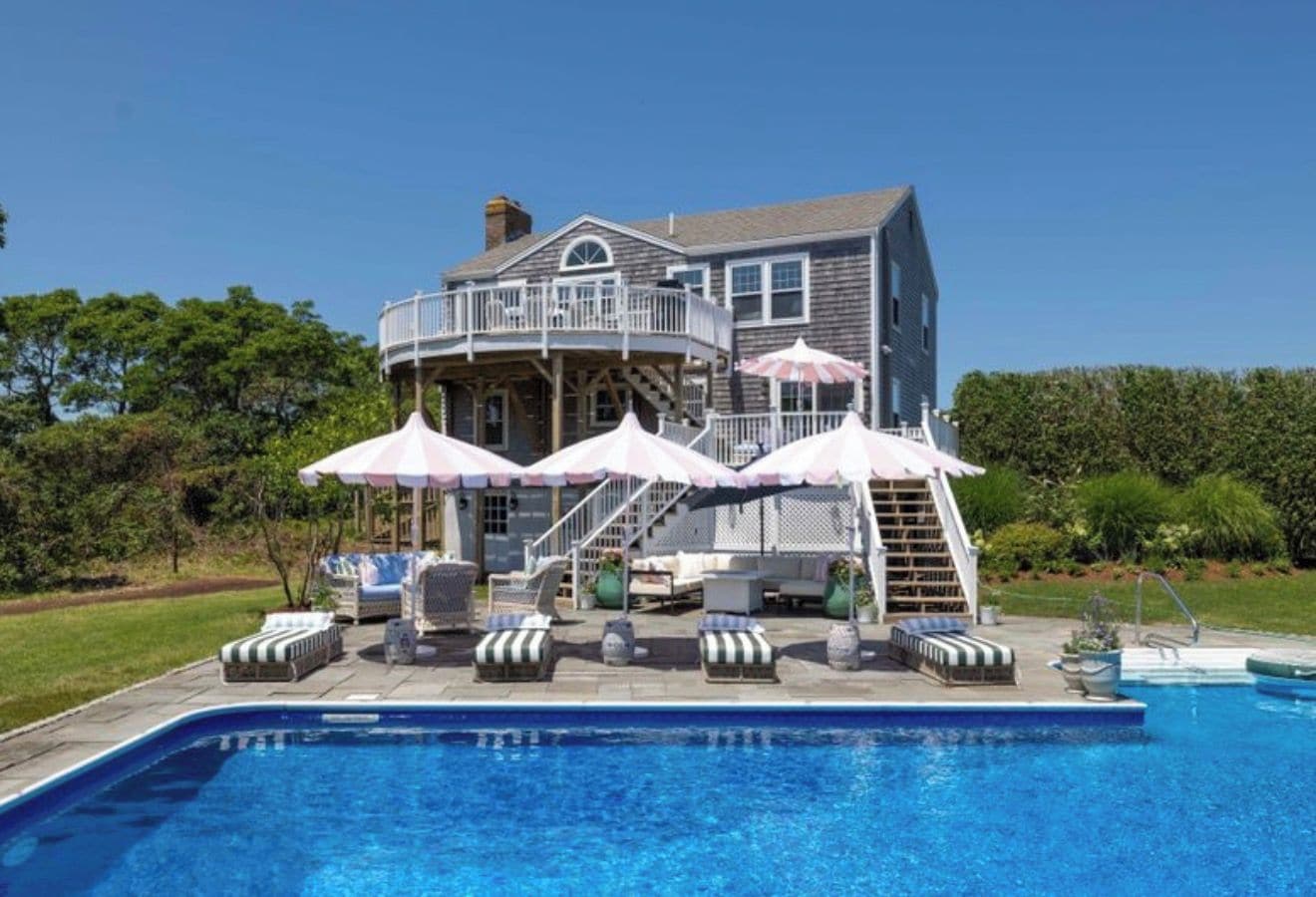 A two-story house with a swimming pool, outdoor furniture, and umbrellas.