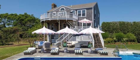 A two-story house with a swimming pool, outdoor furniture, and umbrellas.