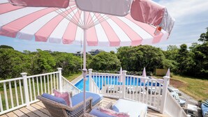 A deck with wicker furniture, a pool, and a white fence. - Longtail Cottage (Nantucket)
