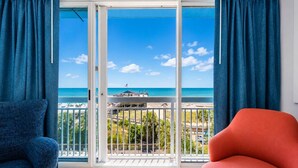 A balcony with a view of the beach, a white-framed window, and a red chair. - Pier & Paradise 2BR Oceanfront Suite Yachtsman 506 (Myrtle Beach)