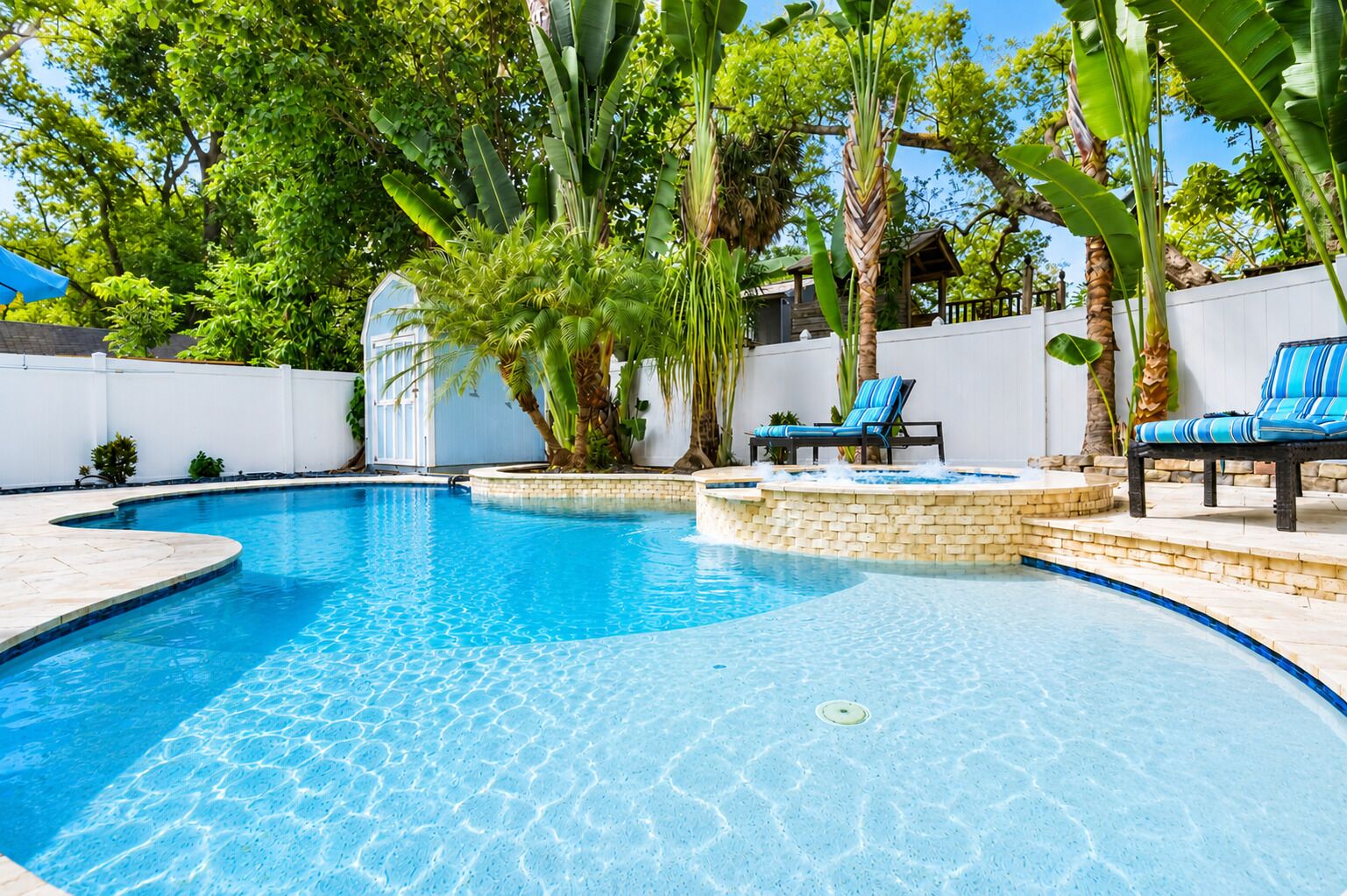 Ein klares Schwimmbecken mit Liegestühlen und tropischer Bepflanzung.