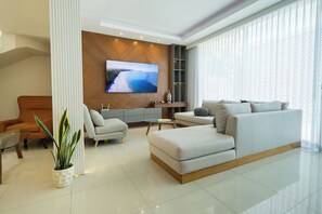 Ein modernes Wohnzimmer mit einem großen Flachbildfernseher an einer Holzwand, einer Couch, einem Couchtisch und einem Topf mit Pflanze.