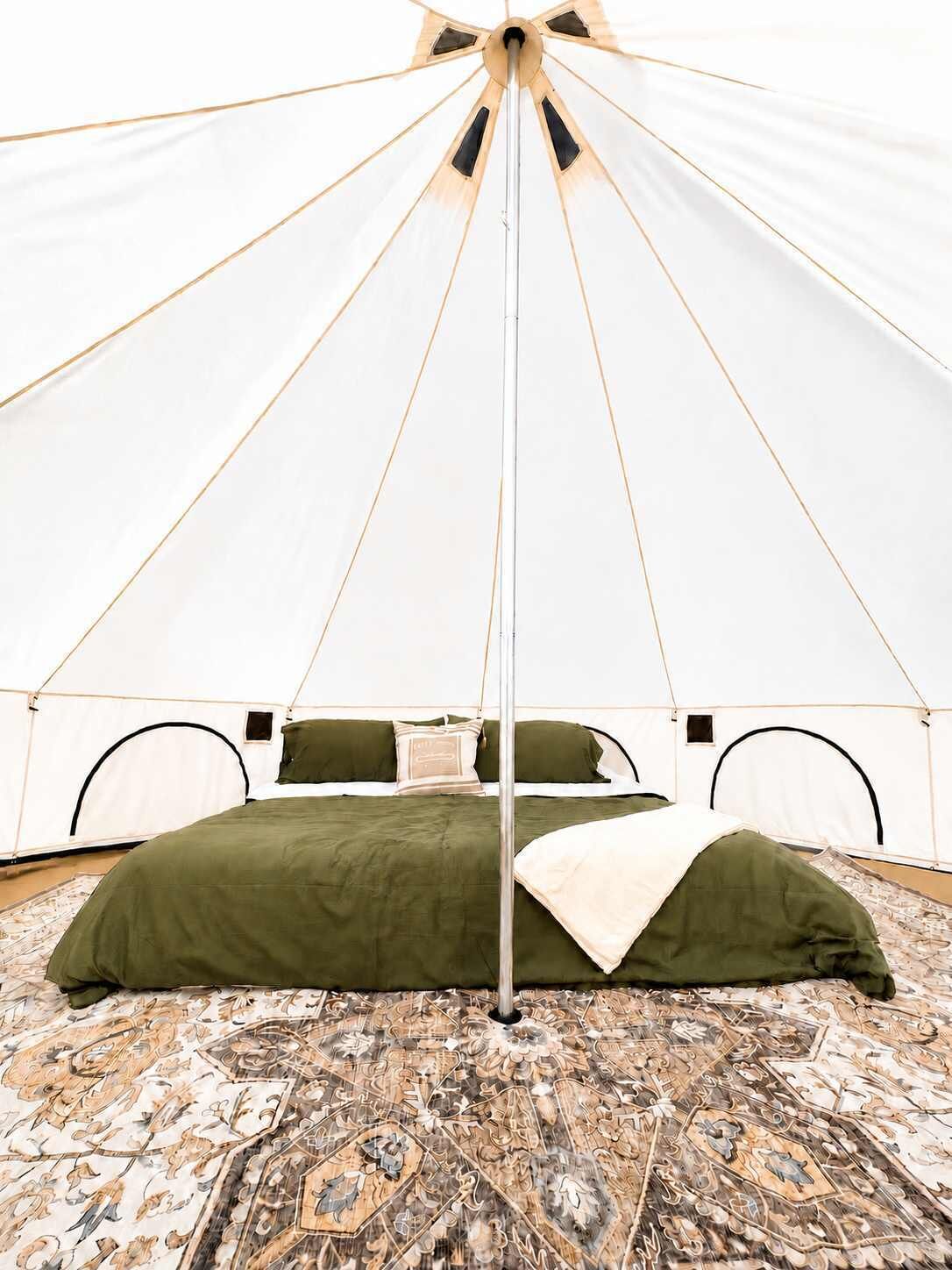 A tent with a bed, pillows, and a patterned rug.
