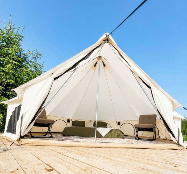Une tente de forme triangulaire, avec deux chaises à l’intérieur et une terrasse en bois.