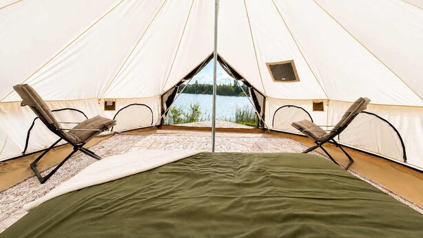 A tent with two chairs and a bed, a view of a lake, and a small window.