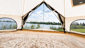 A tent with a view of a lake and forest, a patterned floor, and a small table.