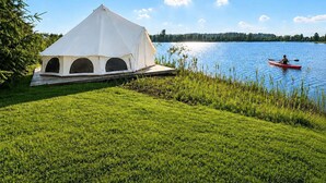 A white tent by a lake with a kayaker in the distance.
