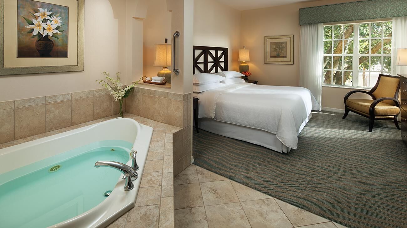 Habitación de hotel con bañera, cama, sillón y ventana con vistas.