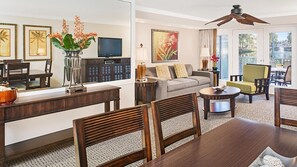 Uma sala de estar com sofá, cadeiras, mesa de centro, televisão, obras de arte nas paredes e uma janela grande.