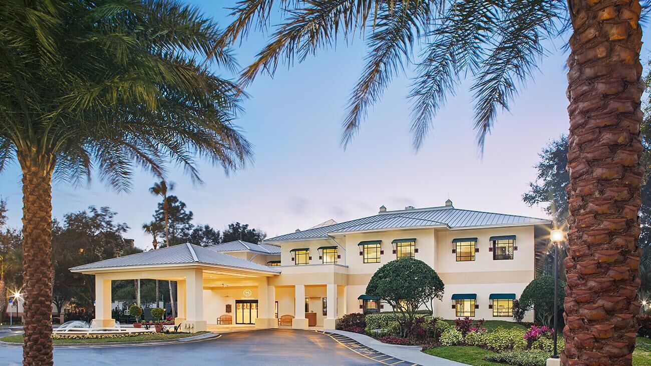 Un hotel grande de dos pisos, con entrada cubierta y un jardín bien cuidado.