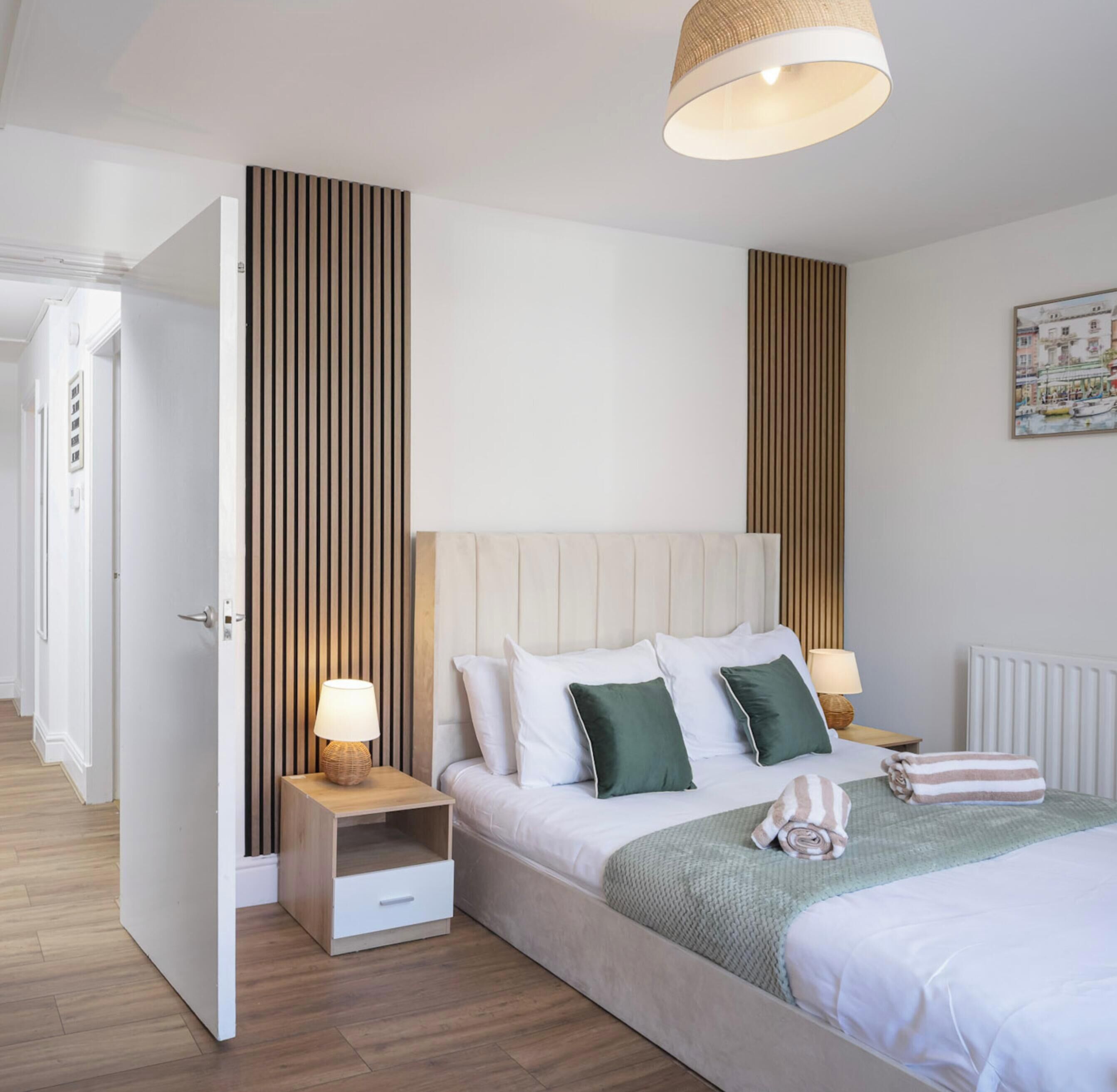 Habitación de hotel con cama, mesitas de noche, lámpara colgante y un cuadro en la pared.