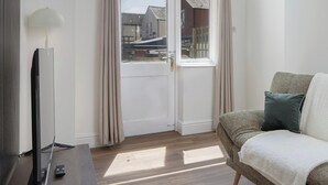 Ein Zimmer mit großem Fenster, einer Couch, einem Flachbildfernseher und einer Lampe.