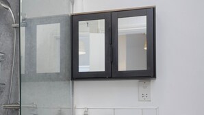 Ein Badezimmer mit einer Duschkabine aus Glas, einem weißen Waschbecken und einem schwarzen Medikamentenschrank.