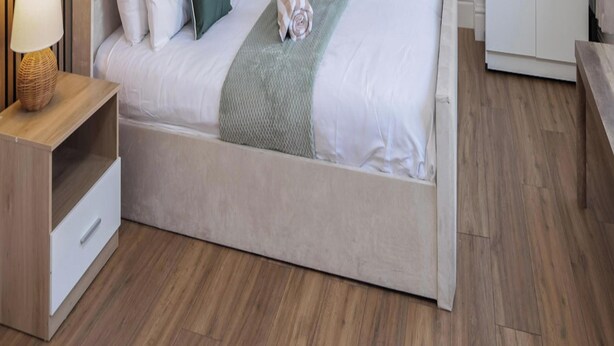 Ein Bett mit Holz-Kopfteil, ein Nachttisch mit Lampe und eine Bank.