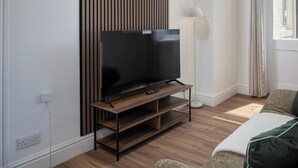 Ein modernes Wohnzimmer mit einem Flachbildfernseher auf einem Holzbodenständer, einer Stehlampe und einem Fenster mit Vorhängen.