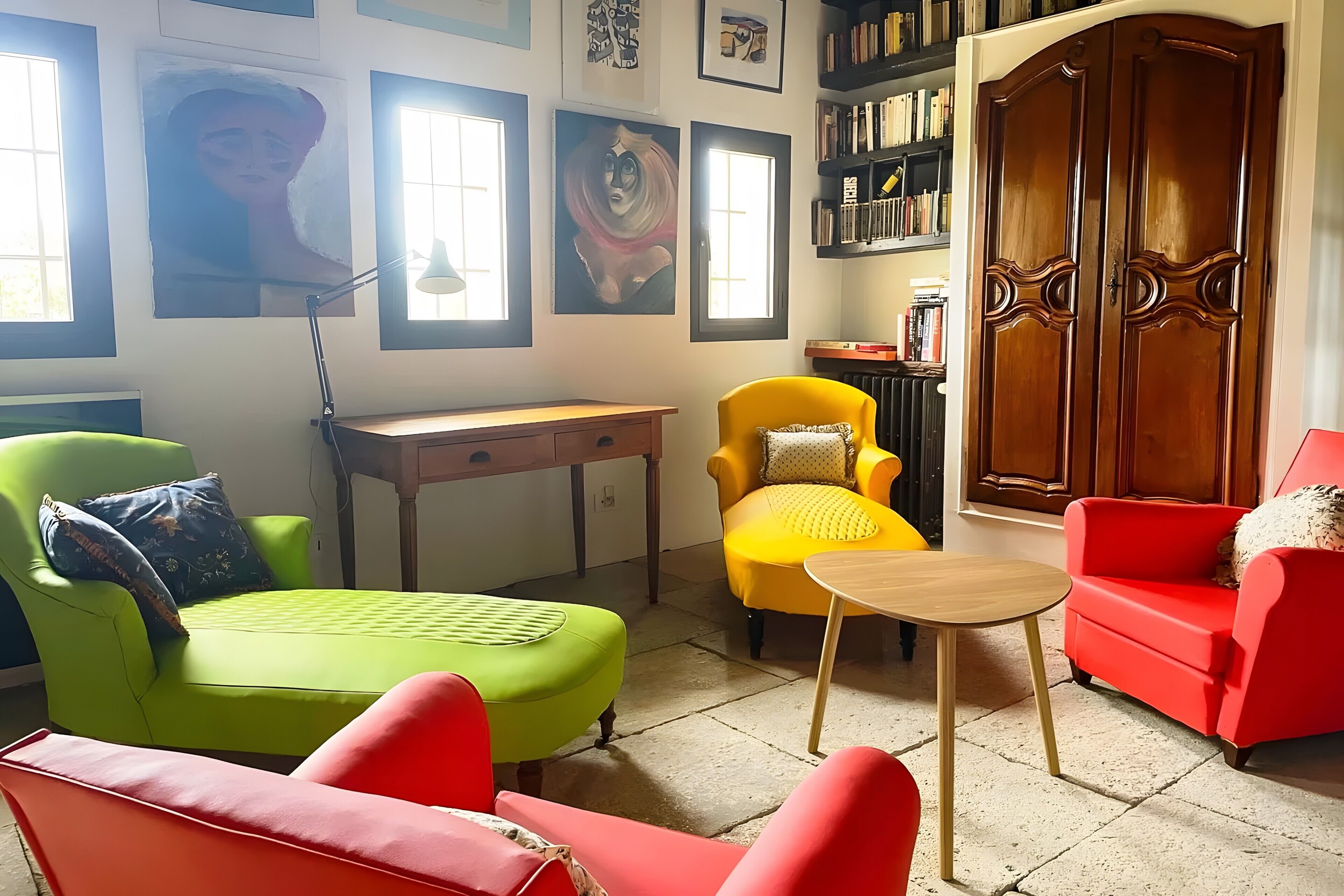 Ein Zimmer mit einem grünen Sofa, einem gelben Sessel, einem roten Sofa, einem Holztisch und einem Bücherregal.