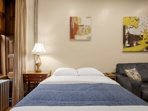 Ein Hotelzimmer mit Bett, Nachttisch, Lampe, Sofa und zwei Bildern an der Wand.