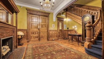 Un amplio pasillo con candelabro, puertas de madera, una escalera y un tapete grande.