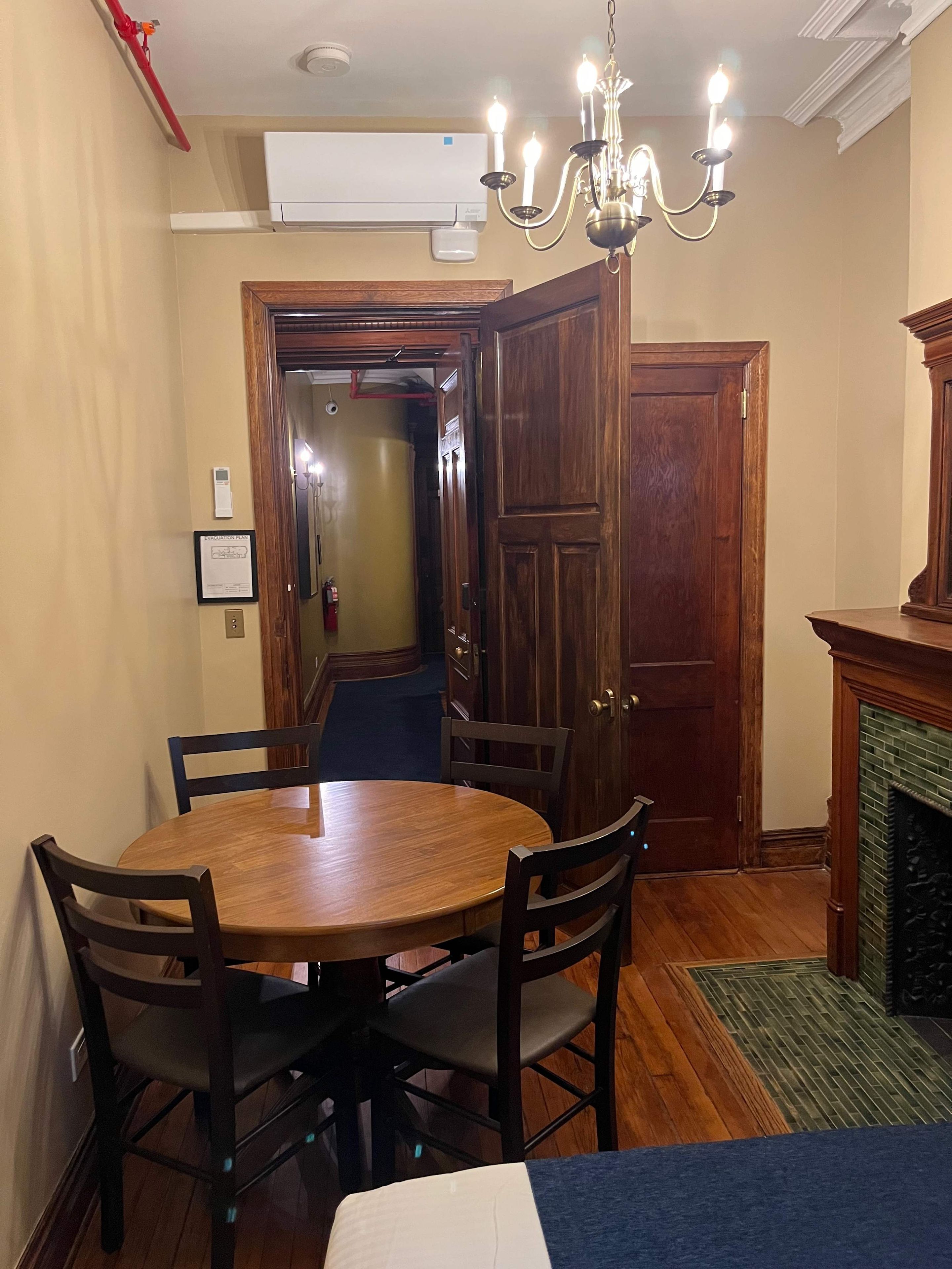 A dining area with a round wooden table, six chairs, a chandelier, and a fireplace.