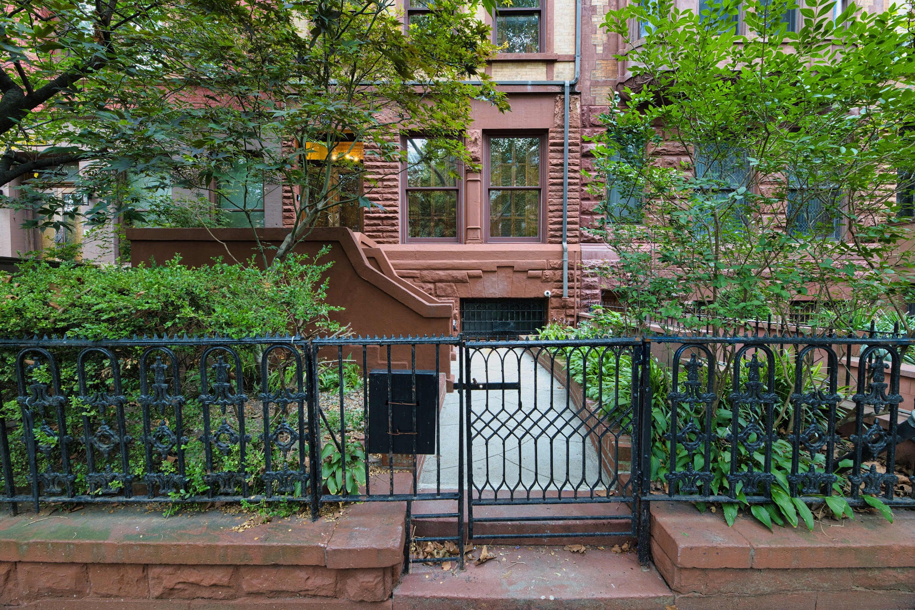 A brick building with a gated entrance, surrounded by greenery and a metal fence.