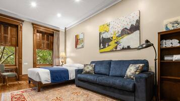 Habitación de hotel con cama, sofá azul, alfombra estampada, un cuadro y estante con toallas.