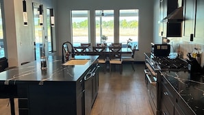 Een moderne keuken met een centraal eiland, donkere kastjes en uitzicht door grote ramen.