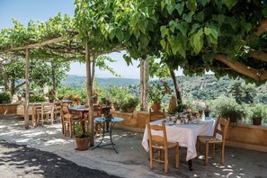 Ein Essbereich im Freien mit Tischen und Stühlen, umgeben von Topfpflanzen und einer Pergola.
