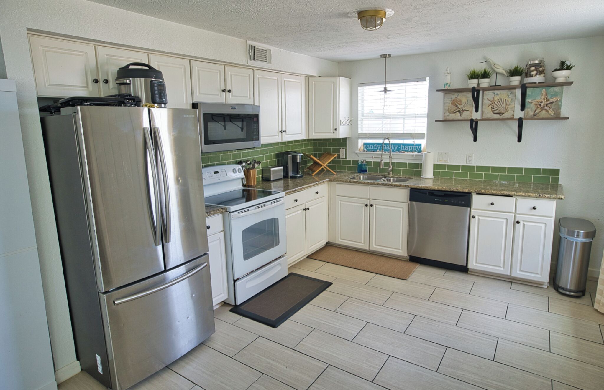 A modern kitchen with white cabinets, stainless steel appliances, a green backsplash, and a small window with a view.