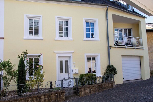 A two-story building with a yellow facade, white-framed windows, a visible garage door, and a small balcony with a metal railing.