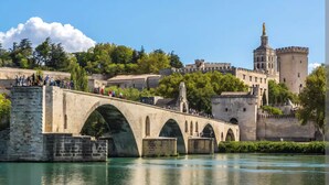 Un ponte in pietra con archi su un fiume, un castello con torri e una statua su una collina.