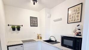 Una cucina compatta con mobili bianchi, lavastoviglie integrata, lavello, forno a microonde e un piccolo piano di lavoro.