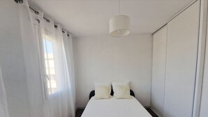 Una camera d'albergo con un letto, tende bianche, un lampadario e una finestra.