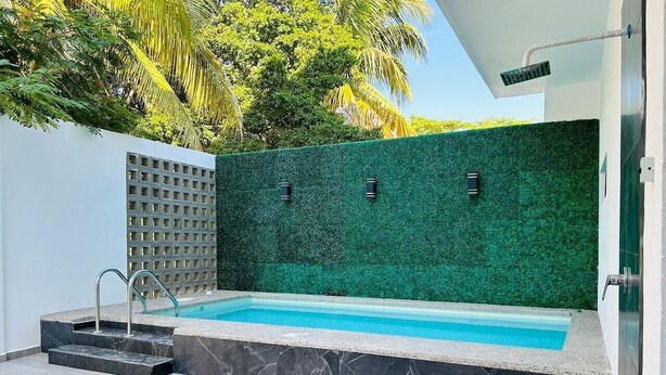 Piscina com parede verde, escada de metal e chão revestido de azulejos.
